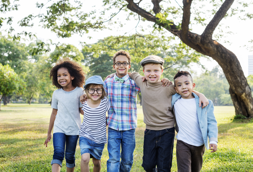 Five smiling kids standing outside with arms around each other's shoulders