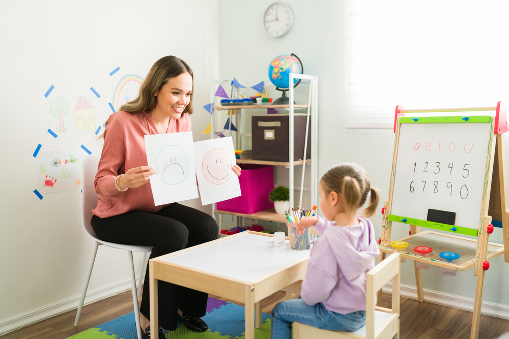 Girl doing SEL activity about identifying feelings with teacher in classroom