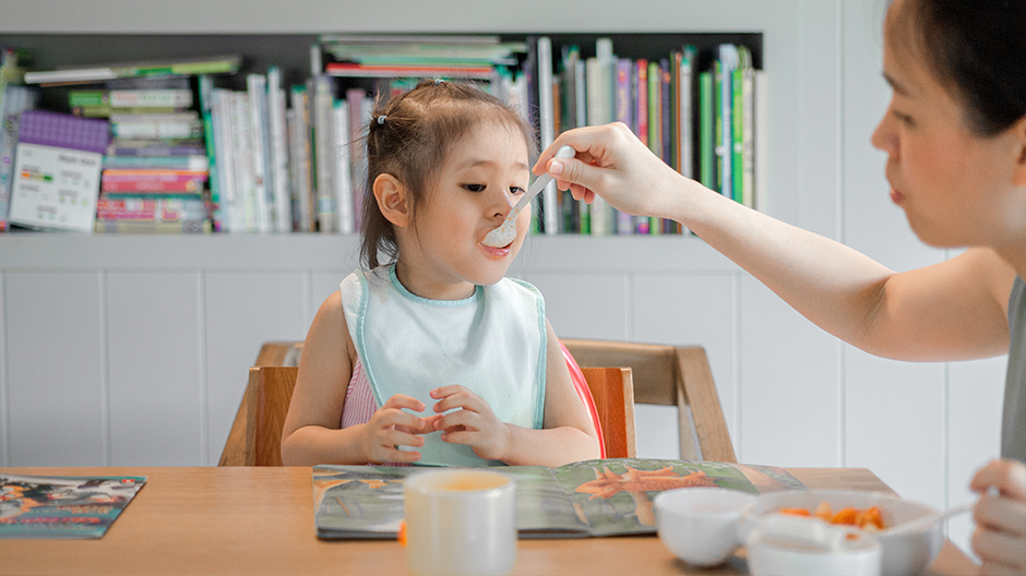 Toddler eating as parent feeds her at table